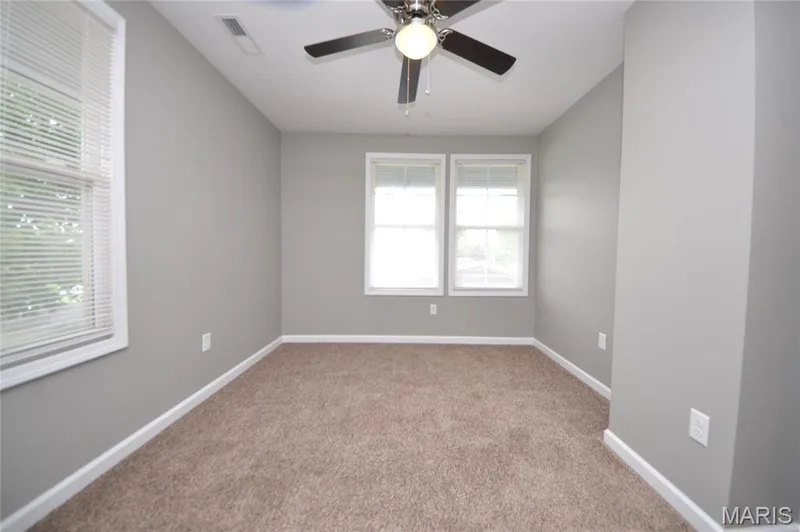 Carpeted room with light grey walls, multiple windows, and a ceiling fan with light fixture — 502 S Linn Avenue, Wentzville, MO 63385