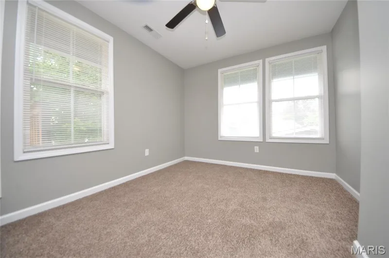 Room featuring light gray walls, white trim, two double-hung windows, and brown carpeting — 502 S Linn Avenue, Wentzville, MO 63385