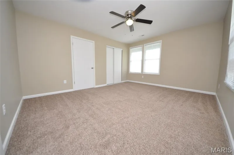 Spacious room featuring neutral carpet flooring, light beige wall paint, white trim, and a ceiling fan with integrated lighting — 502 S Linn Avenue, Wentzville, MO 63385