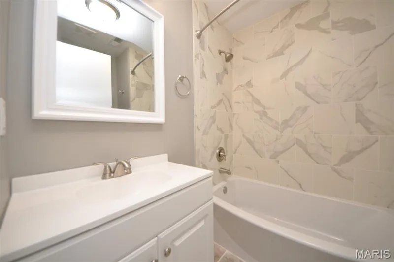 Bathroom featuring a white vanity with integrated sink, brushed nickel faucet, framed mirror, and a tub with surrounding tiled walls — 502 S Linn Avenue, Wentzville, MO 63385