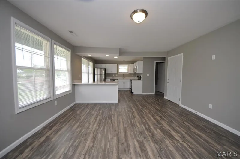 Open-concept living area featuring wood-finish flooring, neutral gray walls, and multiple windows — 502 S Linn Avenue, Wentzville, MO 63385
