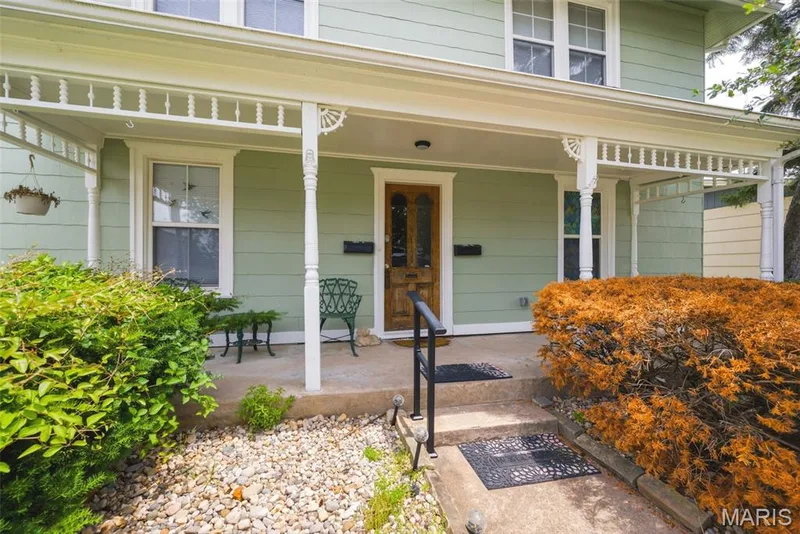 Front porch featuring a wood-paneled entry door, light green siding, and white decorative trim — 502 S Linn Avenue, Wentzville, MO 63385