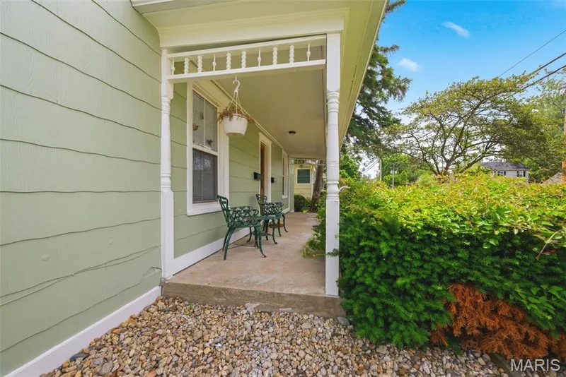 Covered front porch featuring white spindle railings, light green horizontal siding, and a concrete floor — 502 S Linn Avenue, Wentzville, MO 63385