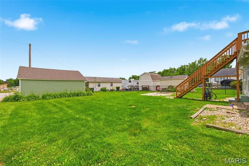 Expansive backyard featuring a large green lawn, a detached garage with green siding, and an exterior wooden staircase — 502 S Linn Avenue, Wentzville, MO 63385
