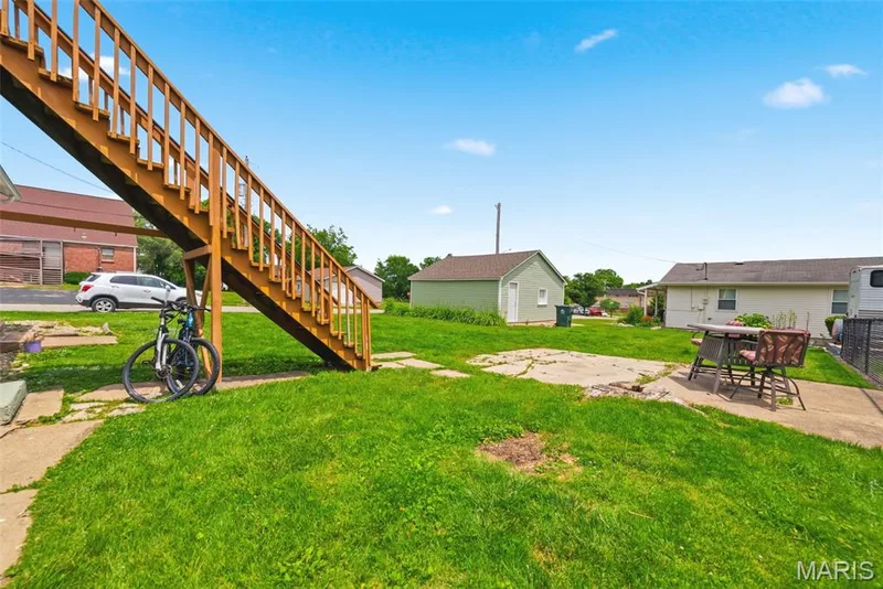 Rear yard featuring a wood exterior staircase, concrete patio, and a separate green outbuilding — 502 S Linn Avenue, Wentzville, MO 63385