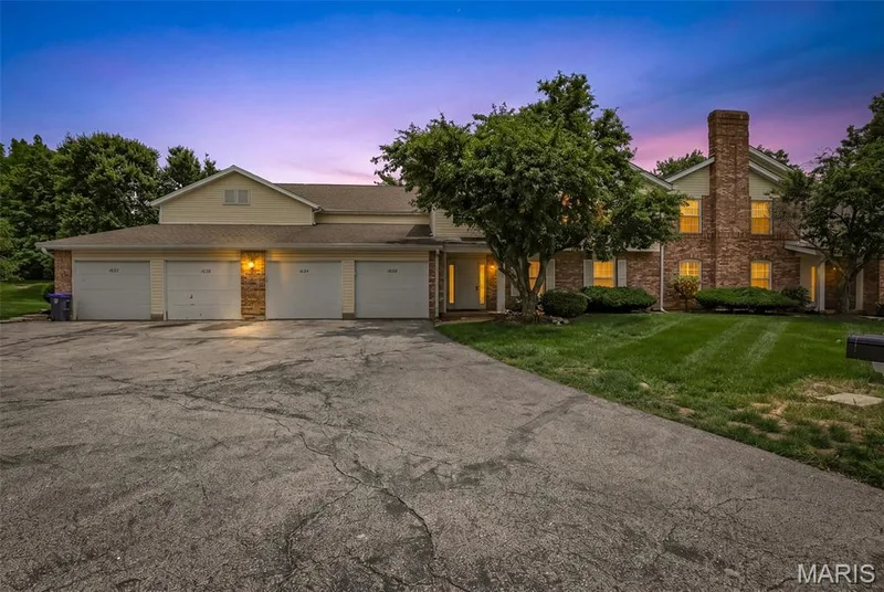 Exterior featuring a combination of brick and siding, a multi-car garage, mature landscaping, and a prominent brick chimney — 1034 Windstream Drive #14, St Peters, MO 63376