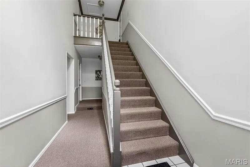 Carpeted staircase featuring a painted wood handrail and balusters, accompanied by a carpeted hallway with chair rail molding and two-tone wall paint — 1034 Windstream Drive #14, St Peters, MO 63376