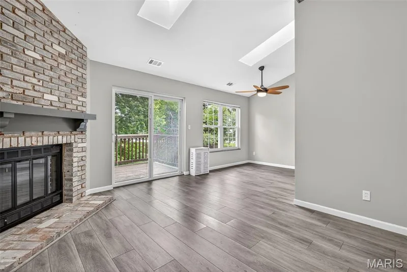 Spacious living area featuring a brick fireplace with a gray mantel, wood-finish flooring, and a vaulted ceiling with skylights — 1034 Windstream Drive #14, St Peters, MO 63376