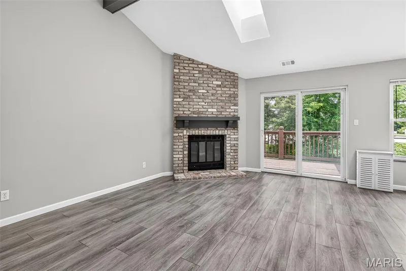 Living area featuring wood-finish flooring, a brick-faced fireplace with a dark wood mantel, and vaulted ceilings with a skylight — 1034 Windstream Drive #14, St Peters, MO 63376