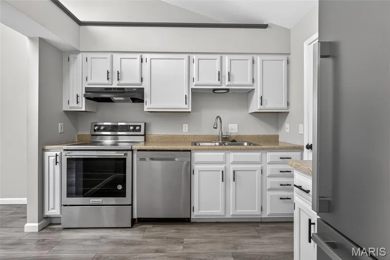 Kitchen featuring white cabinetry with black hardware, stainless steel appliances, stone-finish countertops, and wood-finish flooring — 1034 Windstream Drive #14, St Peters, MO 63376