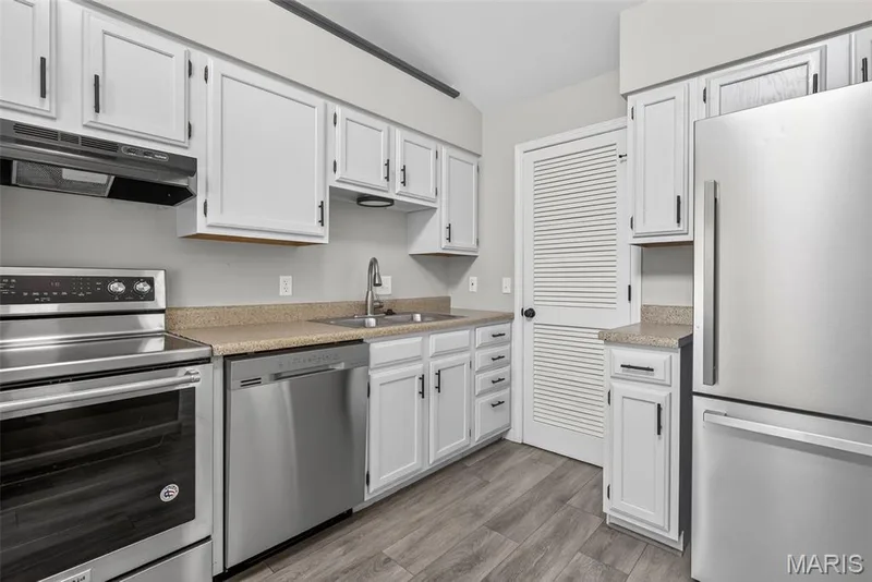 Kitchen featuring white cabinetry with black hardware, stainless steel appliances, wood-finish flooring, and light-toned countertops — 1034 Windstream Drive #14, St Peters, MO 63376
