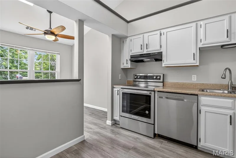 Kitchen area featuring white cabinetry, stainless steel appliances, wood-finish flooring, and a stone-look countertop — 1034 Windstream Drive #14, St Peters, MO 63376