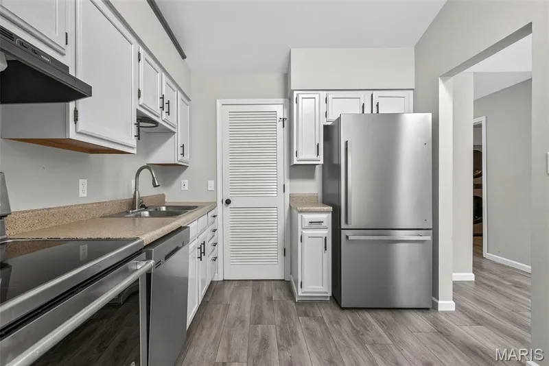 Kitchen featuring white cabinetry with black hardware, stainless steel appliances, speckled countertops, a double basin sink with a gooseneck faucet, and wood-finish flooring — 1034 Windstream Drive #14, St Peters, MO 63376