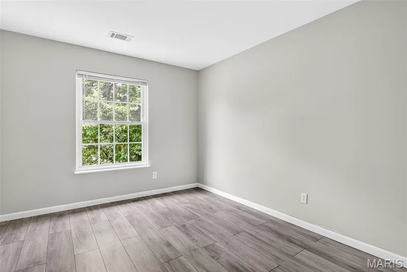 Room featuring light gray walls, wood-finish flooring, white baseboards, and a double-hung window with venetian blinds — 1034 Windstream Drive #14, St Peters, MO 63376