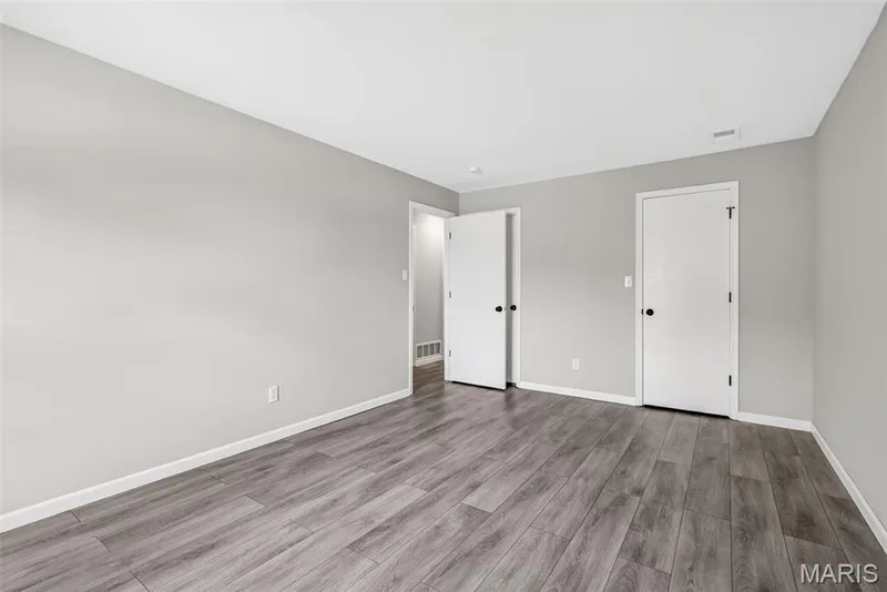 Spacious room featuring wood-finish flooring, light grey painted walls, white baseboards, and white doors with matte black hardware — 1034 Windstream Drive #14, St Peters, MO 63376