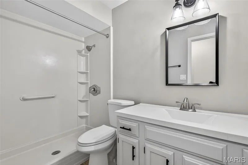 Bathroom featuring a white shower with built-in shelving, white toilet, and a vanity with a white countertop and integrated sink — 1034 Windstream Drive #14, St Peters, MO 63376