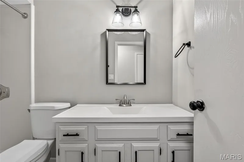 Bathroom vanity featuring a white countertop with an integrated sink, a brushed nickel faucet, and a framed mirror — 1034 Windstream Drive #14, St Peters, MO 63376
