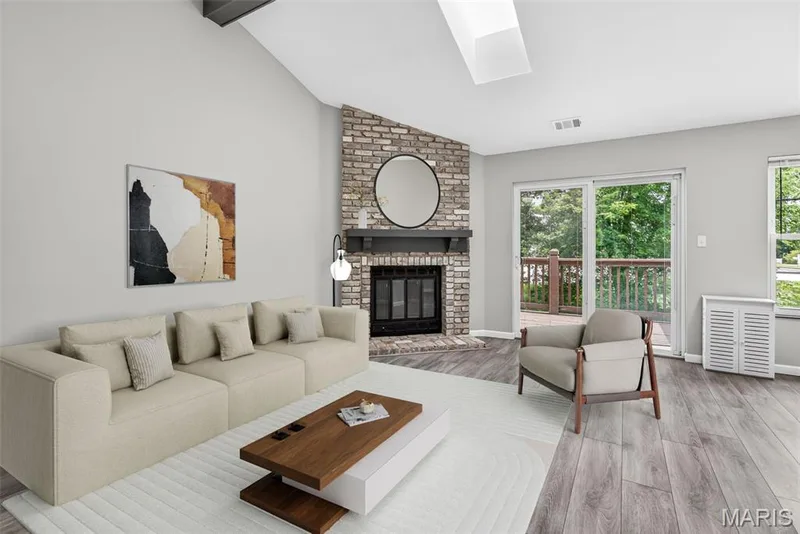Vaulted ceiling with skylight, brick fireplace with dark wood mantle, sliding glass door to exterior deck, wood-finish flooring, and large windows — 1034 Windstream Drive #14, St Peters, MO 63376