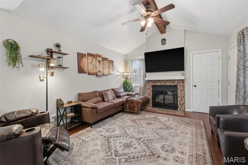 Vaulted ceiling living area featuring wood-finish flooring, a ceiling fan with integrated lighting, coat closet and a fireplace with a tiled surround — 704 Hemingway Lane #E, Weldon Spring, MO 63304