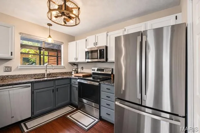 Kitchen featuring garden window, stainless steel appliances, granite countertops, two-tone cabinetry, and wood-finish flooring — 704 Hemingway Lane #E, Weldon Spring, MO 63304
