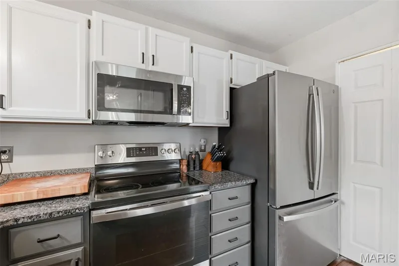 Kitchen featuring stainless steel appliances, granite-style countertops, white upper cabinetry, and gray lower cabinetry — 704 Hemingway Lane #E, Weldon Spring, MO 63304