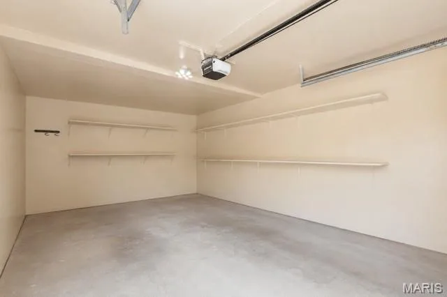 Spacious garage with concrete flooring, integrated shelving, and an automatic garage door opener — 704 Hemingway Lane #E, Weldon Spring, MO 63304