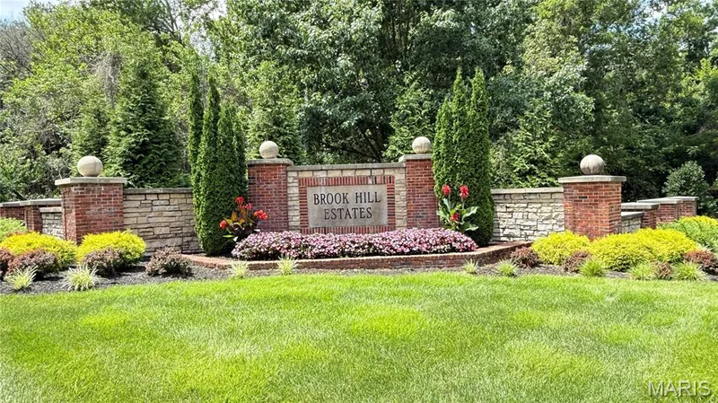 Entrance to subdivision. Brick and stone entry monument featuring an integrated sign, manicured landscaping, and mature trees — 2154 White Lane Drive, Chesterfield, MO 63017