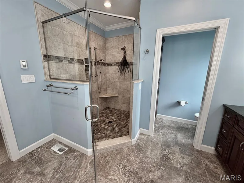 Walk-in shower with clear glass enclosure, tiled walls featuring an accent band, built-in corner bench, and mosaic tile flooring — 2154 White Lane Drive, Chesterfield, MO 63017