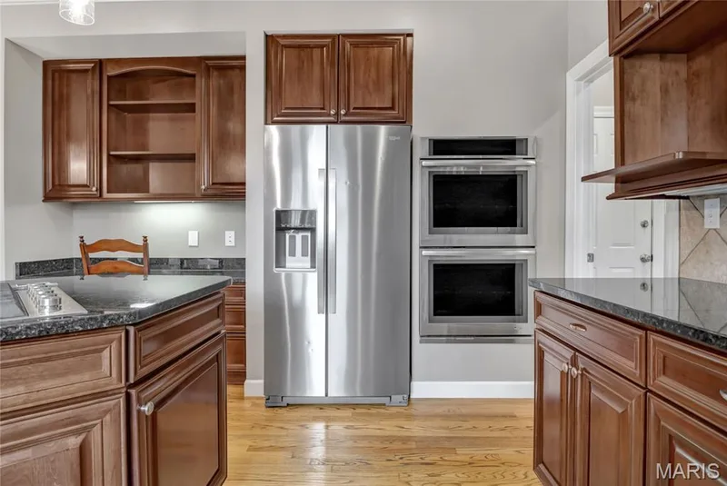 Kitchen featuring a stainless steel side-by-side refrigerator, double wall ovens, rich wood-finish cabinetry, dark countertops, and wood-finish flooring — 2154 White Lane Drive, Chesterfield, MO 63017
