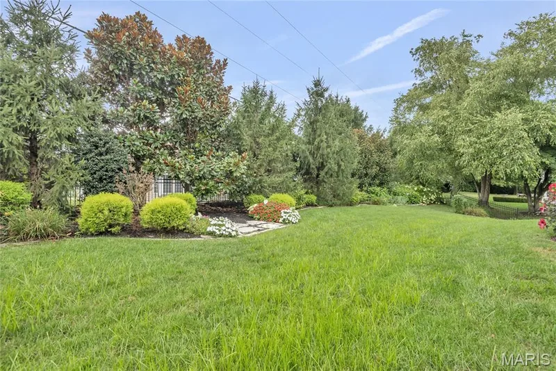 Expansive lawn area featuring mature trees and established shrubbery, complemented by a decorative stone border and planted flowers — 2154 White Lane Drive, Chesterfield, MO 63017
