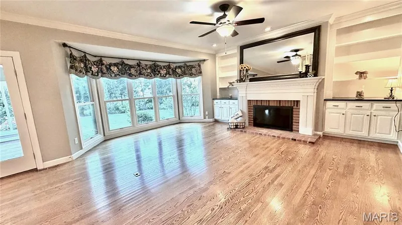 Hardwood flooring, bay window, built-in shelving, fireplace with brick surround, and white cabinetry with dark countertops — 2154 White Lane Drive, Chesterfield, MO 63017