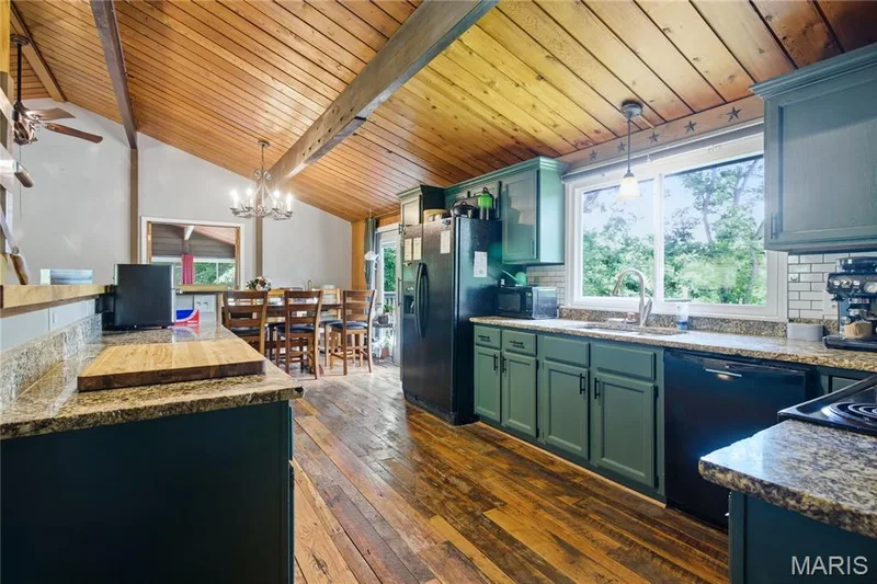 Open-concept kitchen featuring wood-finish flooring, vaulted wood-plank ceiling, exposed wood beams, granite countertops, and painted cabinetry — 1221 Shepard Road, Wildwood, MO 63038