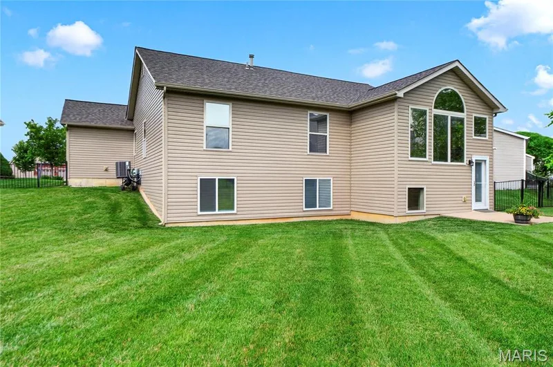 Expansive backyard featuring a manicured lawn, a concrete patio, and a black metal fence — 708 Bellingrath Gardens Court, Wentzville, MO 63385