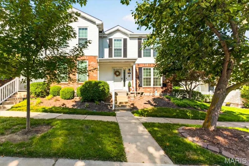 Multistory residence featuring a white siding and brick facade, front entry porch, black louvered shutters, and established landscaping — 115 Carriage View Drive, Wildwood, MO 63040