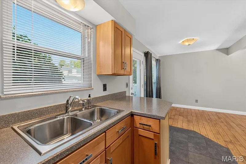 Kitchen featuring wood cabinetry, stainless steel double basin sink, and laminate countertops — 115 Carriage View Drive, Wildwood, MO 63040