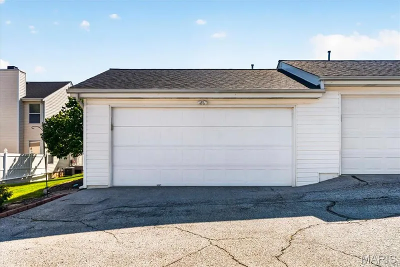 Attached garage featuring a white panel door and exterior lighting — 115 Carriage View Drive, Wildwood, MO 63040