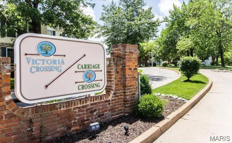 Entryway signage featuring brick masonry, established landscaping, and a curvilinear paved road — 115 Carriage View Drive, Wildwood, MO 63040
