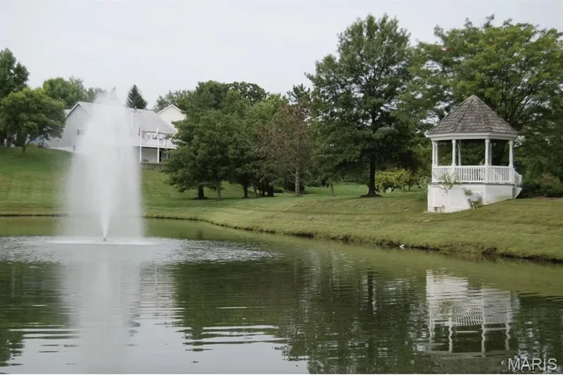 Pond with an active water feature, surrounded by mature trees and a manicured lawn — 115 Carriage View Drive, Wildwood, MO 63040