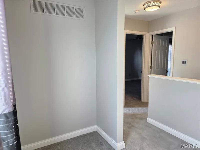 Carpeted hallway featuring light gray walls, white baseboards, and a decorative flush-mount ceiling light — 115 Carriage View Drive, Wildwood, MO 63040