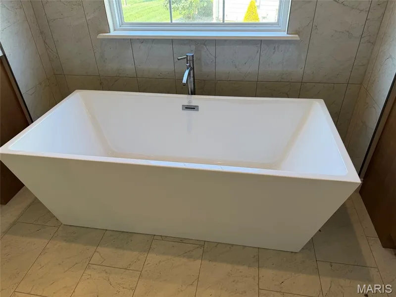Freestanding soaking tub with a chrome floor-mounted faucet, set against a tiled wall and tiled flooring — Lot 27 Bellevaux Place, St Charles, MO 63301
