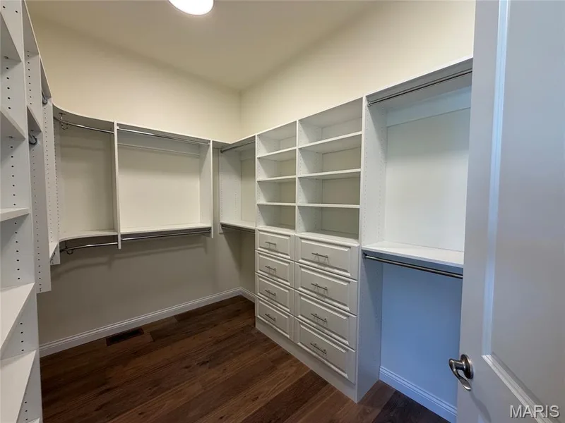Walk-in closet featuring built-in white shelving, integrated drawers with brushed nickel hardware, and wood-finish flooring — Lot 27 Bellevaux Place, St Charles, MO 63301