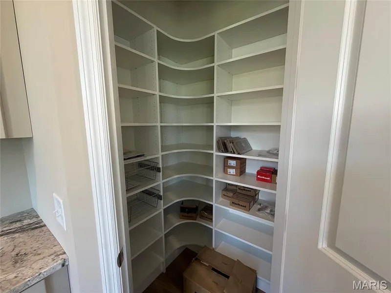 Walk-in pantry with extensive built-in shelving, curved corner shelving, wood-finish flooring, and pull-out wire baskets — Lot 27 Bellevaux Place, St Charles, MO 63301