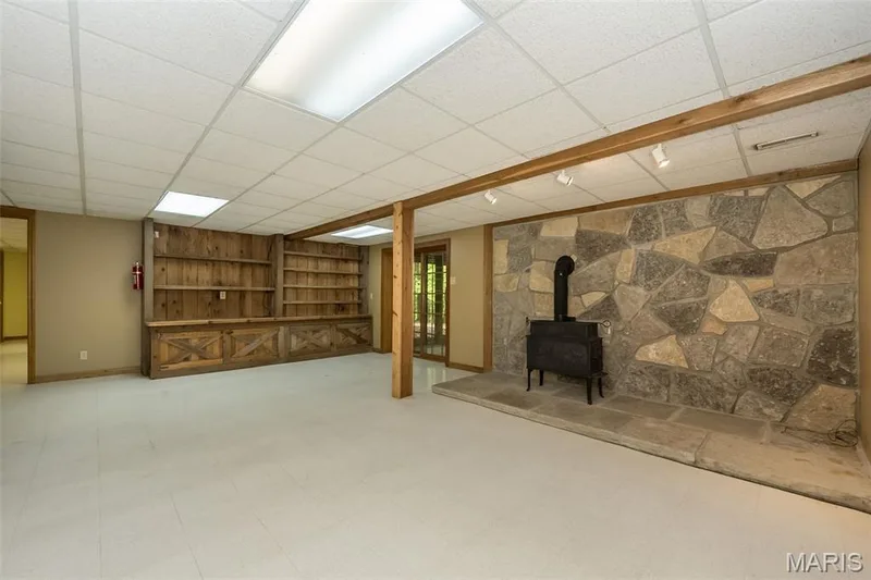 Below grade area with built in features, baseboards, a wood stove, a paneled ceiling, and tile patterned floors — 2731 Christy Avenue, Wildwood, MO 63040