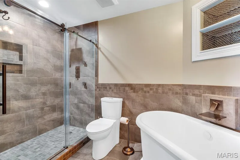 Bathroom featuring a freestanding white bathtub, a walk-in shower with glass enclosure, tiled walls, and recessed lighting — 309 Hemingway Lane, Weldon Spring, MO 63304
