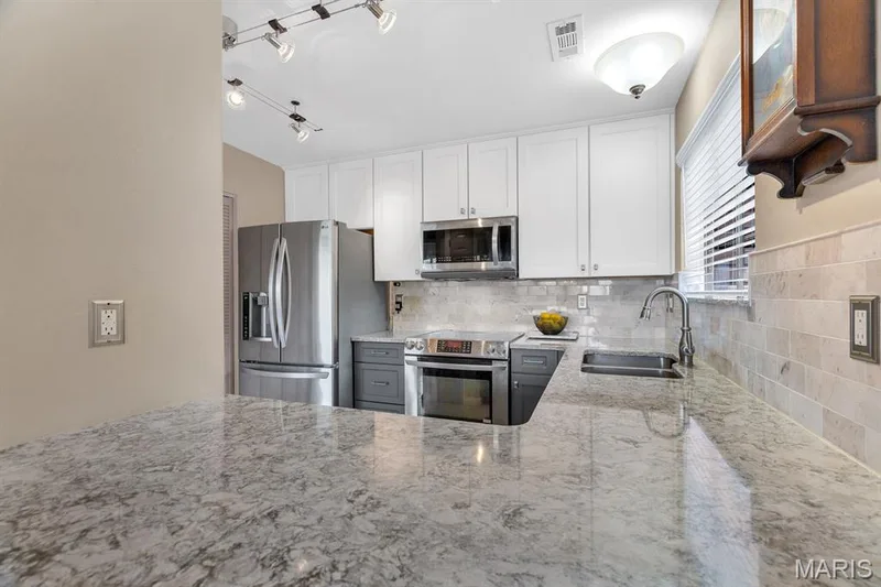 Kitchen featuring Cambria quartz countertops, white upper cabinetry, gray lower cabinetry, a stainless steel refrigerator, and a tile backsplash — 309 Hemingway Lane, Weldon Spring, MO 63304