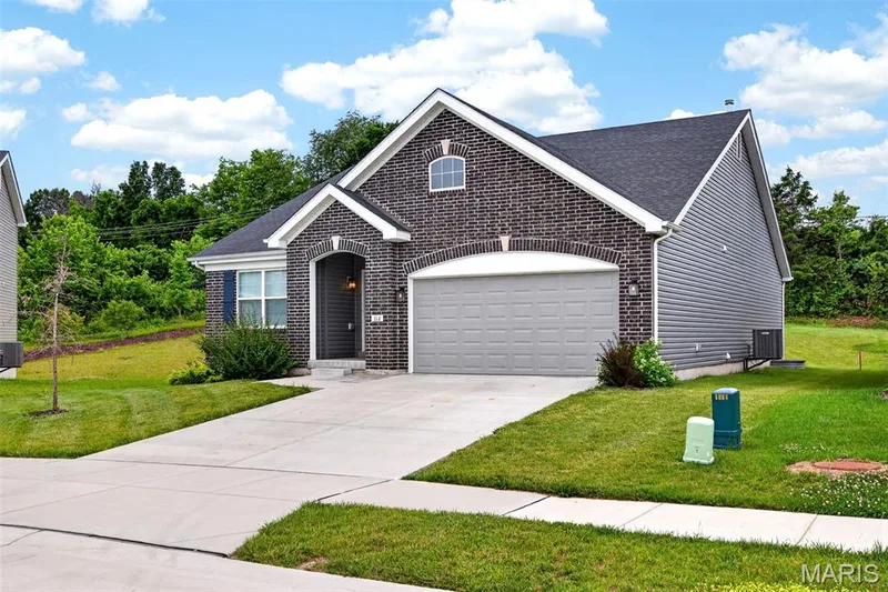 Single-story residence featuring a brick facade with arch detailing, a two-car garage, and gray siding accents — 112 Creek Haven Court, Lake St. Louis, MO 63367