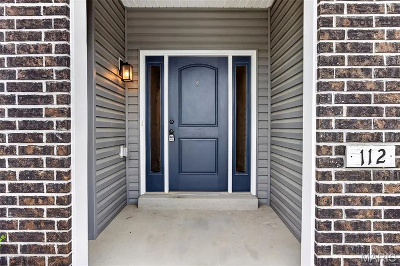 Entryway featuring a paneled door with sidelights, brick facade, horizontal siding, and an exterior wall lantern — 112 Creek Haven Court, Lake St. Louis, MO 63367