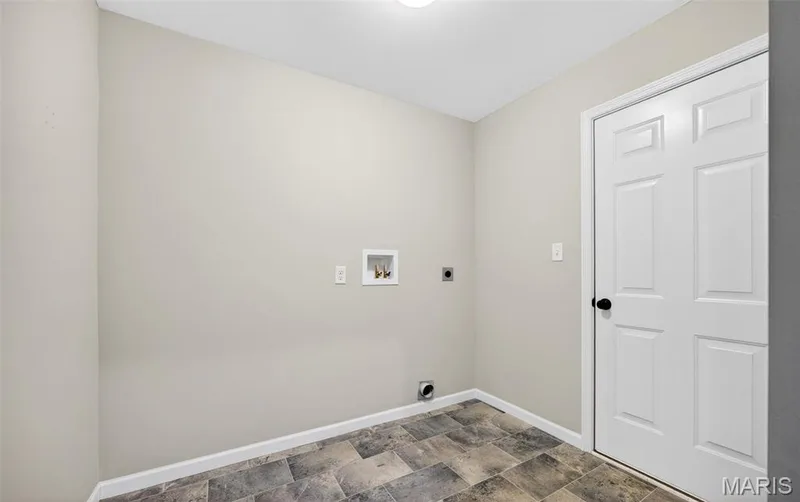 Utility area featuring light neutral walls, a white six-panel door with black hardware, and patterned floor tiling — 112 Creek Haven Court, Lake St. Louis, MO 63367