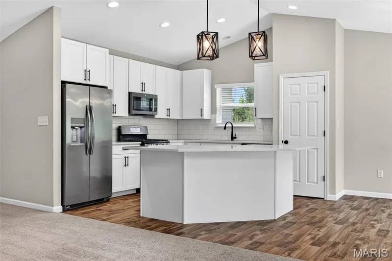 Bright kitchen featuring white cabinetry, stainless steel appliances, a center island, vaulted ceiling with recessed lighting, and wood-finish flooring — 112 Creek Haven Court, Lake St. Louis, MO 63367