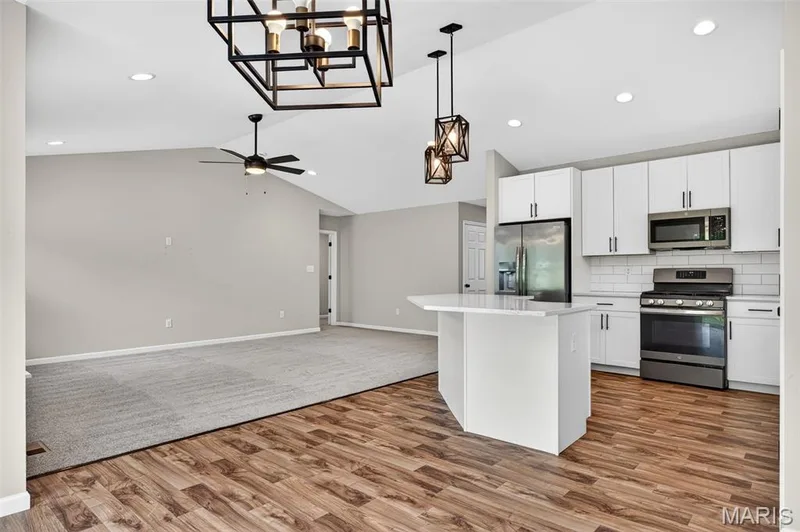 Open-concept kitchen and living area featuring wood-finish flooring, white cabinetry, stainless steel appliances, and a central island with a solid surface countertop — 112 Creek Haven Court, Lake St. Louis, MO 63367
